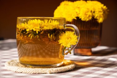 Dandelion flower healthy tea in glass cup on table. Herbal medicine Delicious tisane tea from with fresh yellow blossom dandelion flowers inside tea cup. Green clearing infusion Wildflowers Eco