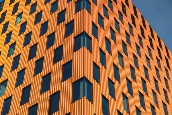 Modern office building exterior with glass facade on clear sky background. Transparent glass wall of office building with orange decoration. Element of facade of modern European building Commercial