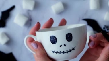 Female hands paint on white cup scary jacks face DIY for kids Halloween home activities Holiday art children craft Handmade decorations. Socially distanced at home Idea for art class