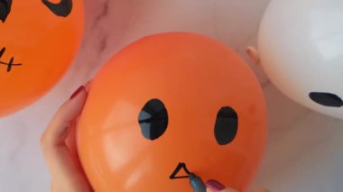 Female hands painting Jacks face on balloons. Orange and white balls preparation diy for halloween party. Halloween home activities. Handmade toys Children craft