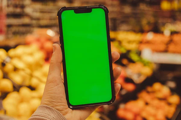 Mobile phone Chroma key. Close up of woman hand holds smart phone with green screen at shopping mall store. Buying food at supermarket, grocery shop center online. Department store. Gadgets