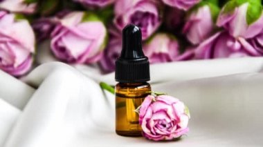 Gül yağını 4 km yakınlaştır. Spa ve aromaterapi gül çiçekleri saten şampanya rengi kumaş pipetli gerekli yağ şişesi. Bir şişe gül yağı ve taze çiçekler..