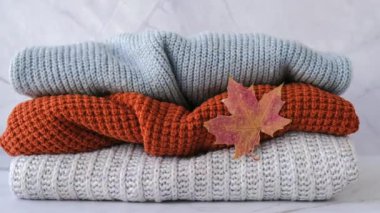 4k yakınlaştır. Sonbahar akçaağaç yaprağıyla örülmüş sıcak süveter yığını. Eski moda süveterler. Turuncu ve mavi renkler. Samimi kızlık zarı konsepti Sonbahar sezonu