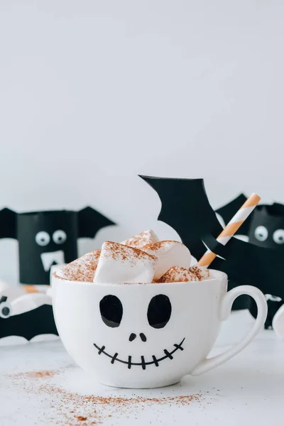 Painted white cup scary jacks face with marshmallows Hot chocolate cacao drink DIY for kids. Halloween home activities Holiday art children craft Handmade decorations home Idea for art class.