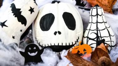 4k zoom in out Halloween background with painted face pumpkins and autumn leaves. Diy. Do it yourself. Halloween decorations, black and white pumpkins, bats, ghosts. Halloween party greeting card