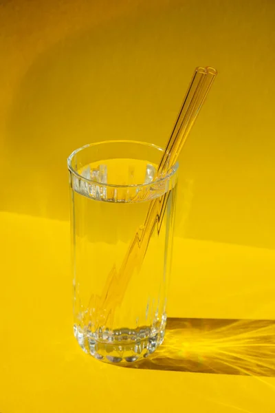 Reusable glass Straws in Glass with water on yellow background Eco-Friendly Drinking Straw Set with cleaning brush. Zero waste, plastic free concept. Sustainable lifestyle. Waste free living Low waste