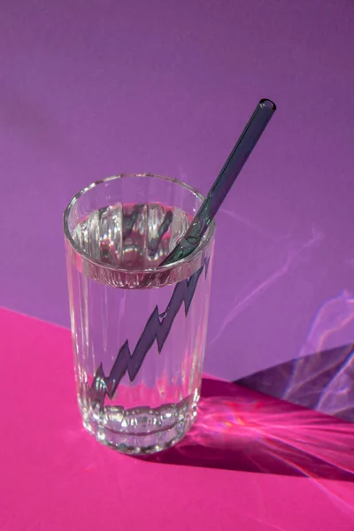 Reusable glass Straws in Glass with water on purple violet background Eco-Friendly Drinking Straw Set with cleaning brush. Zero waste, plastic free concept. Sustainable lifestyle. Waste free living
