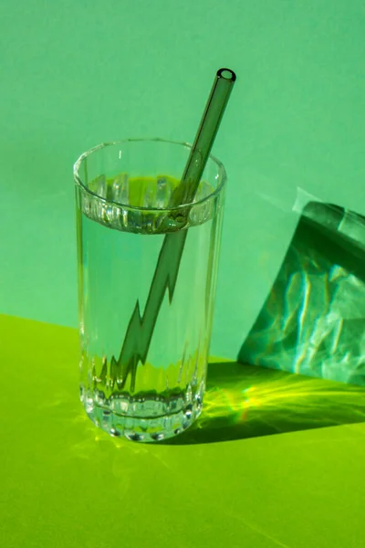Reusable glass Straws in Glass with water on green background Eco-Friendly Drinking Straw Set with cleaning brush. Zero waste, plastic free concept. Sustainable lifestyle. Waste free living Low waste