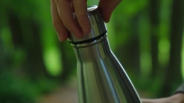 Tanımlanamayan bir kadının su şişesini tuttuğu yakın plan. Temiz su döküyorum. Parka yeniden kullanılabilir çelik termo su şişesi döküyorum. Sürdürülebilir yaşam tarzı. Plastiksiz sıfır atıksız yaşam. Bastır yeşil