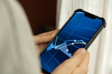 Kadın eli telefonu tutuyor, borsa grafiğini kontrol ediyor ve güvenlik değiş tokuşuna yatırım yapıyor. Telefonu tutan kadın, hisse senedi ekranını göster. Borsa yatırım kavramı Muhasebe