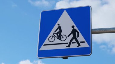 Bisikletçi ve yaya yolu paylaşım tabelası. Yol tabelası yayalar ve bisikletler mavi gökyüzünün arka planında karşıdan karşıya geçebilirler.