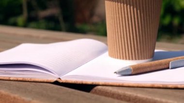 Parktaki ahşap bankta çalışma kavramı. Kağıt bardaktan kahve içmek. Öğrenci ev ödevi yapıyor. Not defterine kadın elleri yazıyor. Minnettarlık günlüğü.