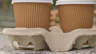 Çay için kapaklı iki kağıt bardak. Masadan kahve al. Kahverengi kağıt bardak tutacağı olan kahve. Kahverengi güvenlik kartonundan tasmalar. Bardaklar için paket götür. Karton tepsi