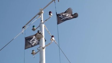 Jolly Roger veya korsan gemisi bayrağı dalgalanırken bayrak direği ve mavi gökyüzü, kafatası ve çapraz kemikler, Karayip Korsanları ve Siyah İnci. Yırtılmış yırtık eski kumaş dokusu