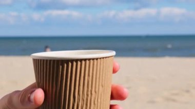 Denizin arka planında tek kullanımlık bir fincan çay. Çay bir kağıt bardağa doldurulur. Kadın elleri termo-şişeden sıcak çay dolduruyor ve dışarıda kalmaktan zevk alıyor. Doğayla birlik