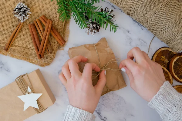 Woman making Box with New Year's gifts, wrapped in craft paper and decorated with cinnamon sticks. Holidays and Gifts concept. Handmade Eco friendly alternative green Christmas presents zero waste Sustainable lifestyle Top view