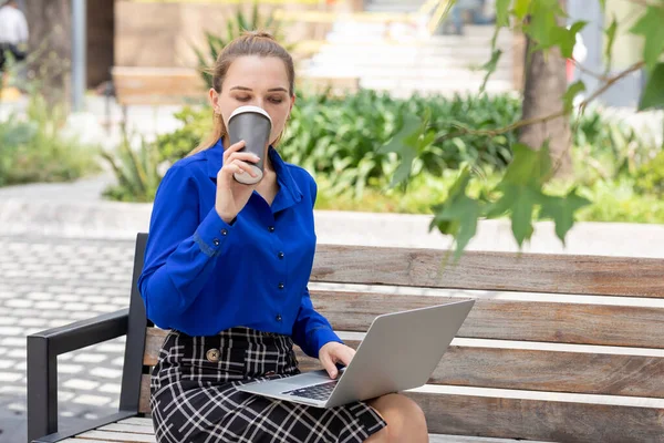 Femeia executivă bea cafea dintr-un pahar în timp ce lucra pe laptop stând pe o bancă de stradă — Fotografie, imagine de stoc