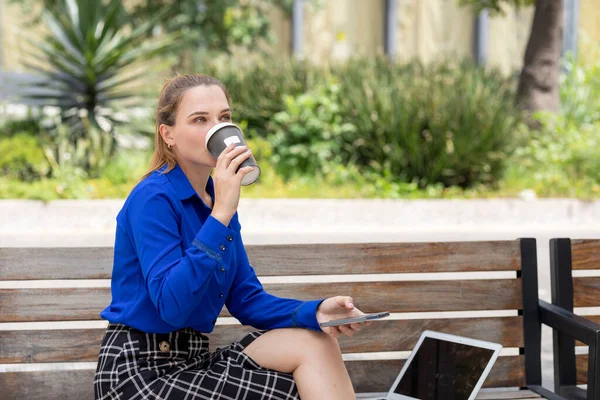 Femeia executivă bea cafea dintr-un pahar în timp ce lucra pe laptop stând pe o bancă de stradă — Fotografie, imagine de stoc