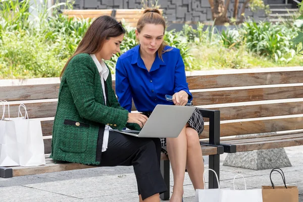 Doi tineri directori de sex feminin verificarea laptop-ul lor în timp ce chat după cumpărături, cu saci de cumpărături — Fotografie, imagine de stoc