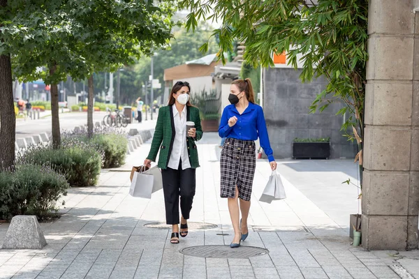 İki genç kadın sokakta maske takarak yürüyorlar. Alışveriş yaptıktan sonra ellerinde poşetlerle bir bardak kahveyle mutlu mesut konuşuyorlar.