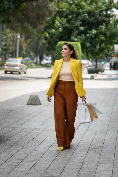 Sokaklarda alışveriş torbalarıyla dolaşan genç ve mutlu bir kadın.