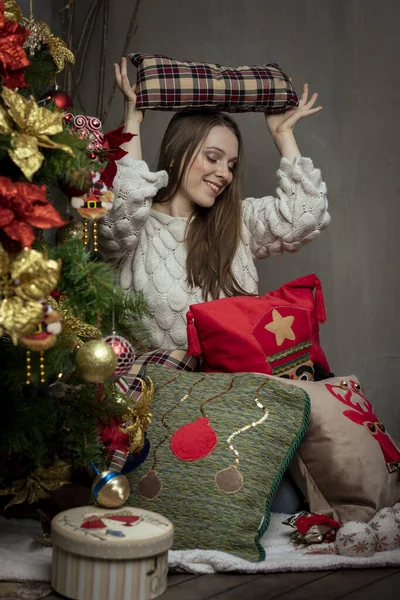 Junge kaukasische Frau lächelt neben einem Weihnachtsbaum mit Weihnachtskissen — Stockfoto