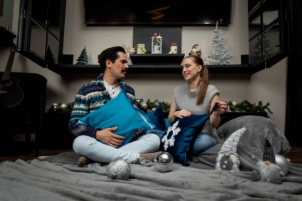 Junges Paar plaudert fröhlich in seinem Wohnzimmer mit Kissen und einer Decke in einer Weihnachtsnacht — Stockfoto