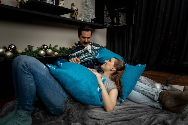 Junge verliebte Männer und Frauen sitzen mit Kissen und Weihnachtsdekoration auf dem Fußboden in ihrem Wohnzimmer — Stockfoto