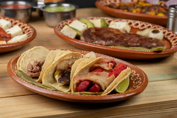 Drie taco 's geserveerd op een kleiplaat vergezeld van salsa en citroenen op een houten tafel — Stockfoto