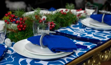 Noel yemeği için mavi Noel süslemeli, çanak çömlekli ve camlı bir masa.