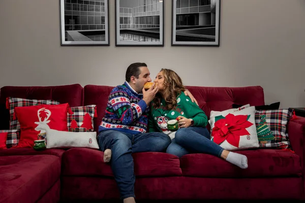 Lateinisches Paar zu Weihnachten beim Brotessen im Wohnzimmer mit Weihnachtsdekoration und Bildern an der Wand — Stockfoto