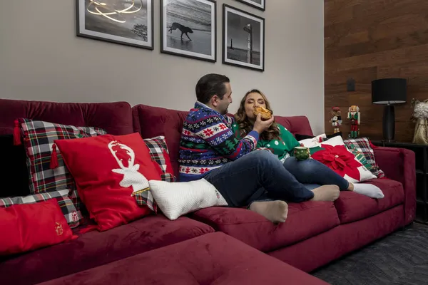 Lateinisches Paar zu Weihnachten beim Brotessen im Wohnzimmer mit Weihnachtsdekoration und Bildern an der Wand — Stockfoto