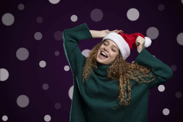 Junge Frau mit fröhlichem Gesichtsausdruck, Weihnachtsmütze und Weihnachtspullover, mit Lichtern im Hintergrund — Stockfoto