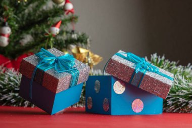 Arkasında Noel ağacı olan mavi fiyonklu hediyeler.