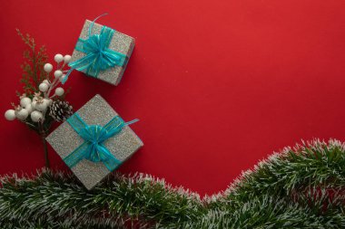 Mavi fiyonklu, yeşil dallı ve kırmızı arka planlı hediye kutularıyla Noel arkaplanı