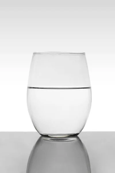 Kristályüveg vízzel és fehér háttér szürke gradienssel — Stock Fotó