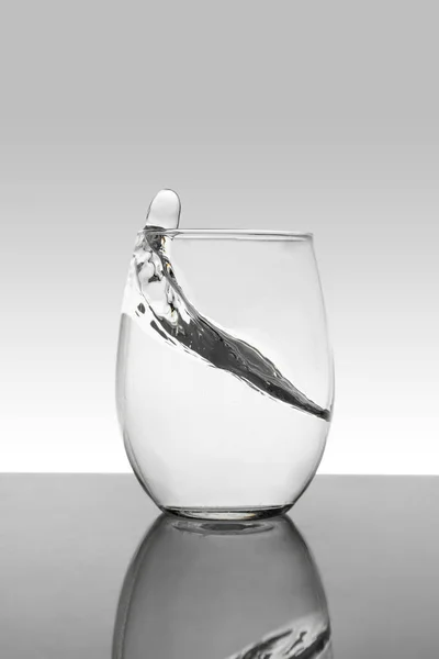 Cristal con agua en movimiento y fondo blanco con gradiente gris — Foto de Stock
