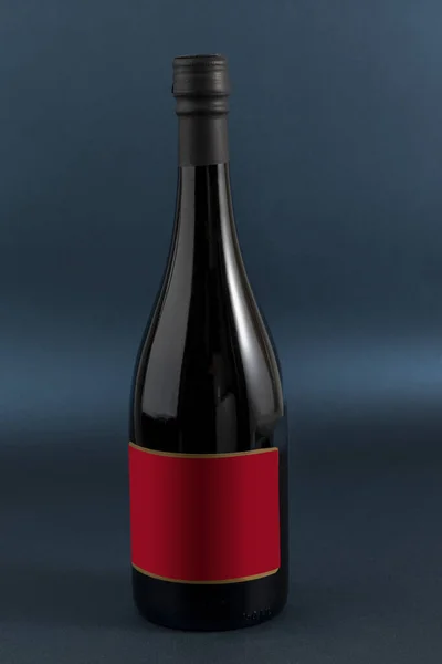 Botella de vino con etiqueta roja para texto o marca, y un fondo de color azul — Stock fotografie