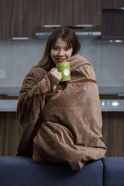 Vertical portrait of Woman with cold covered with a blanket at home, having a cup of coffee — Stock fotografie