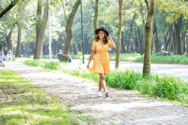 Woman in yellow dress walks along the sidewalk in a park