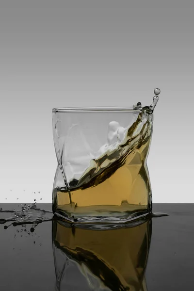 Vertical portrait splash of whiskey in crystal glass with gradient background — Zdjęcie stockowe