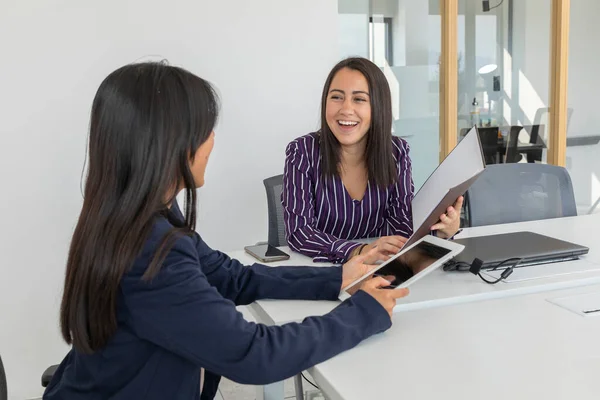 İki genç Latin iş kadını bir ofiste iş belgelerini gözden geçiriyorlar. Yönetici kadınlar önemli evrakları imzalıyorlar.