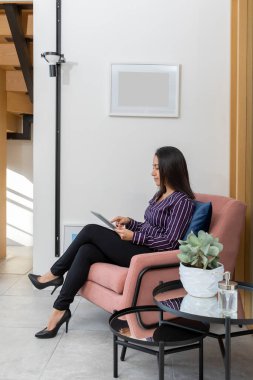 Resmi olarak sandalyede tabletle oturan, lobide beklerken çalışan bir kızın yan görünüşü..