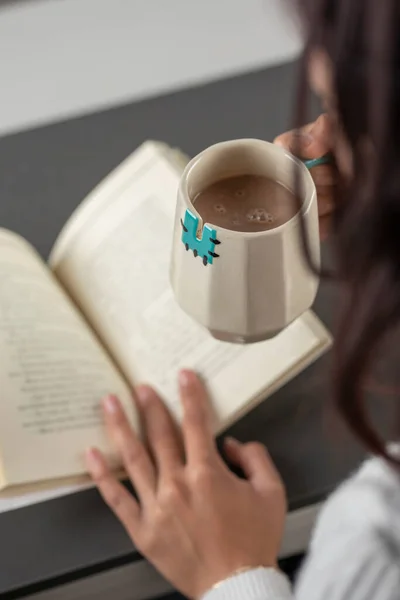 Toma vertical de una mujer latina sosteniendo una taza de café, mientras lee un libro por la mañana — Foto de Stock
