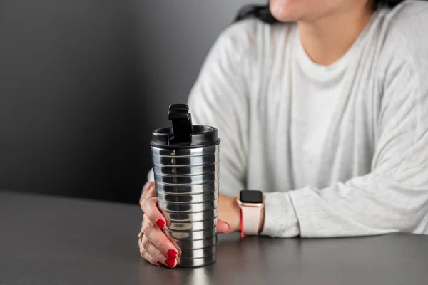 Elinde alüminyum termosla masada dinlenen bir kadın.