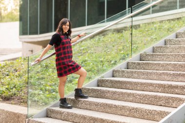 Merdivenlere dayanmış kırmızı elbiseli ve fotokopi çeken bir kadın.