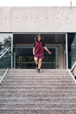 Neşeli Latin kadın hızla bir binanın merdivenlerinden aşağı iniyor.