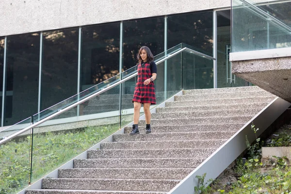 Kırmızı elbiseli genç Latin kadın fotokopi odası olan bir binanın merdivenlerinden aşağı iniyor.