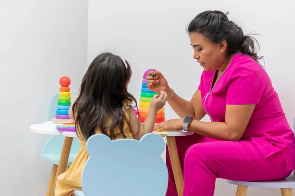 Latina vrouwelijke kinderarts zitten met een meisje patiënt tekening aan een kindertafel in haar kantoor — Stockfoto