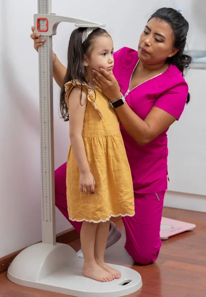 拉丁美洲的儿科医生在她的办公室里给一个女孩量尺寸 她有一把基座尺子 — 图库照片